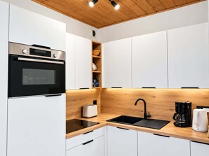 A modern kitchen with white cabinets, a black oven, a wooden countertop, a sink, and a coffee maker.