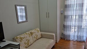 A living room with a sofa, a television, a wardrobe, and a window with sheer curtains. - Stadion apt 2 Near Athens city center (Athina)