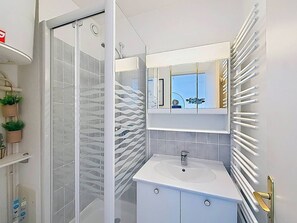 Un baño con cabina de ducha de vidrio, un lavabo blanco y un espejo con un diseño decorativo de azulejos en la pared.