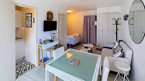 A compact room with a kitchenette, a dining area, a bed, and a mirror. - Sea-View Studio with Balcony, Private Parking & Bikes - Sleeps 4 (Merville-Franceville-Plage)