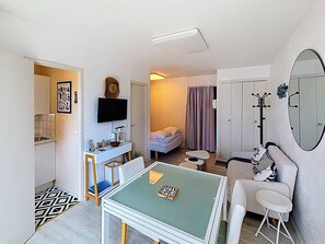 A compact room with a kitchenette, a dining area, a bed, and a mirror.