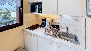 A compact kitchen with white cabinets, a microwave, a coffee maker, and a sink. - Sea-View Studio with Balcony, Private Parking & Bikes - Sleeps 4 (Merville-Franceville-Plage)