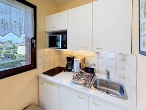 A compact kitchen with white cabinets, a microwave, a coffee maker, and a sink.