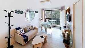 A compact living space with a sofa, dining table, and a coat rack. - Sea-View Studio with Balcony, Private Parking & Bikes - Sleeps 4 (Merville-Franceville-Plage)