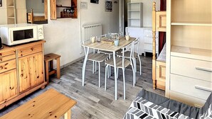 Un espace de vie compact comprenant une table à manger en bois, des chaises blanches, un four à micro-ondes et une petite kitchenette.