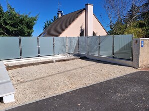 Ein von einer Mauer umgebener Weg führt zu einem Gebäude mit einem geneigten Dach und einem Schornstein.
