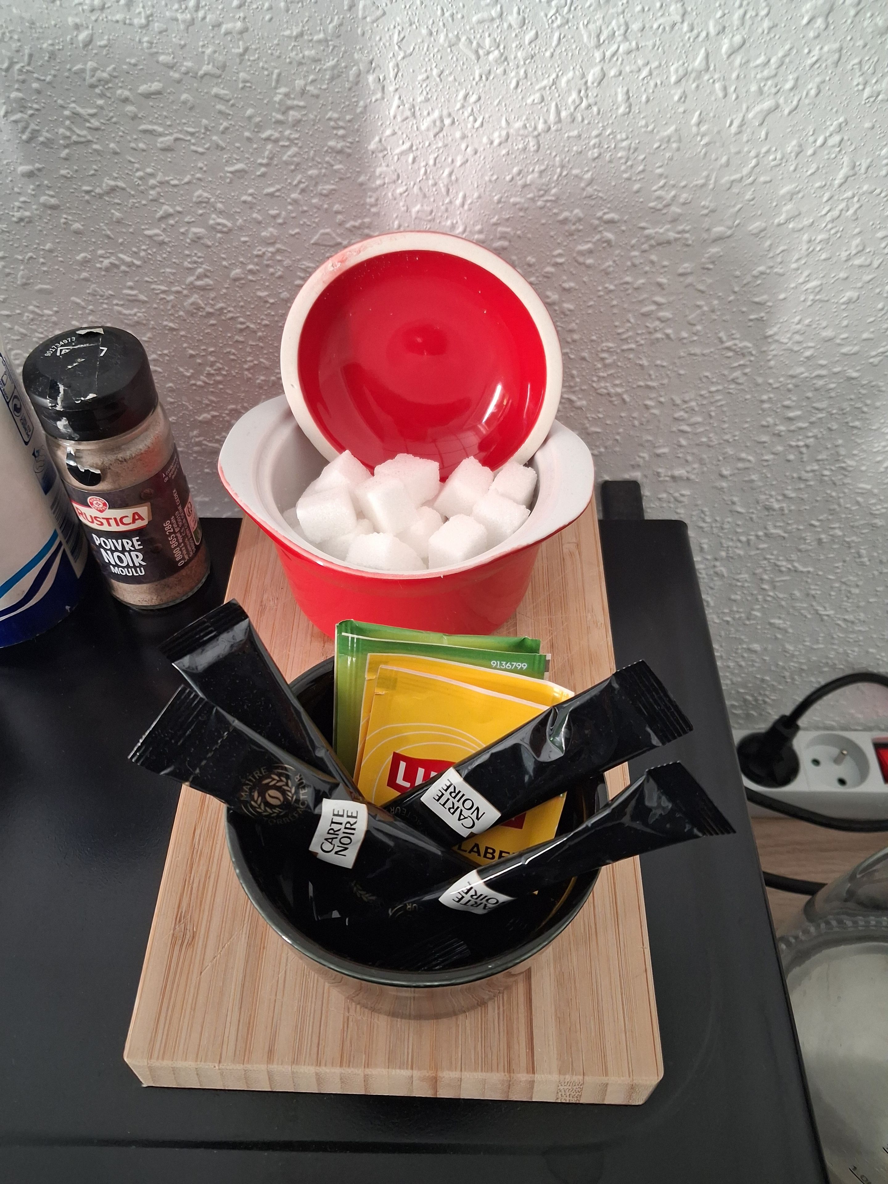 Een aanrecht met een rode kom, daarin suikerklontjes, een fles kruiden en boterzakjes.