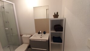 Un bany amb dutxa de vidre, un vàter, un lavabo amb mirall i una petxina amb tovalloles doblegades.