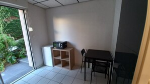 Una habitació petita amb terra de rajola, un armari blanc, una cadira negra i una taula.