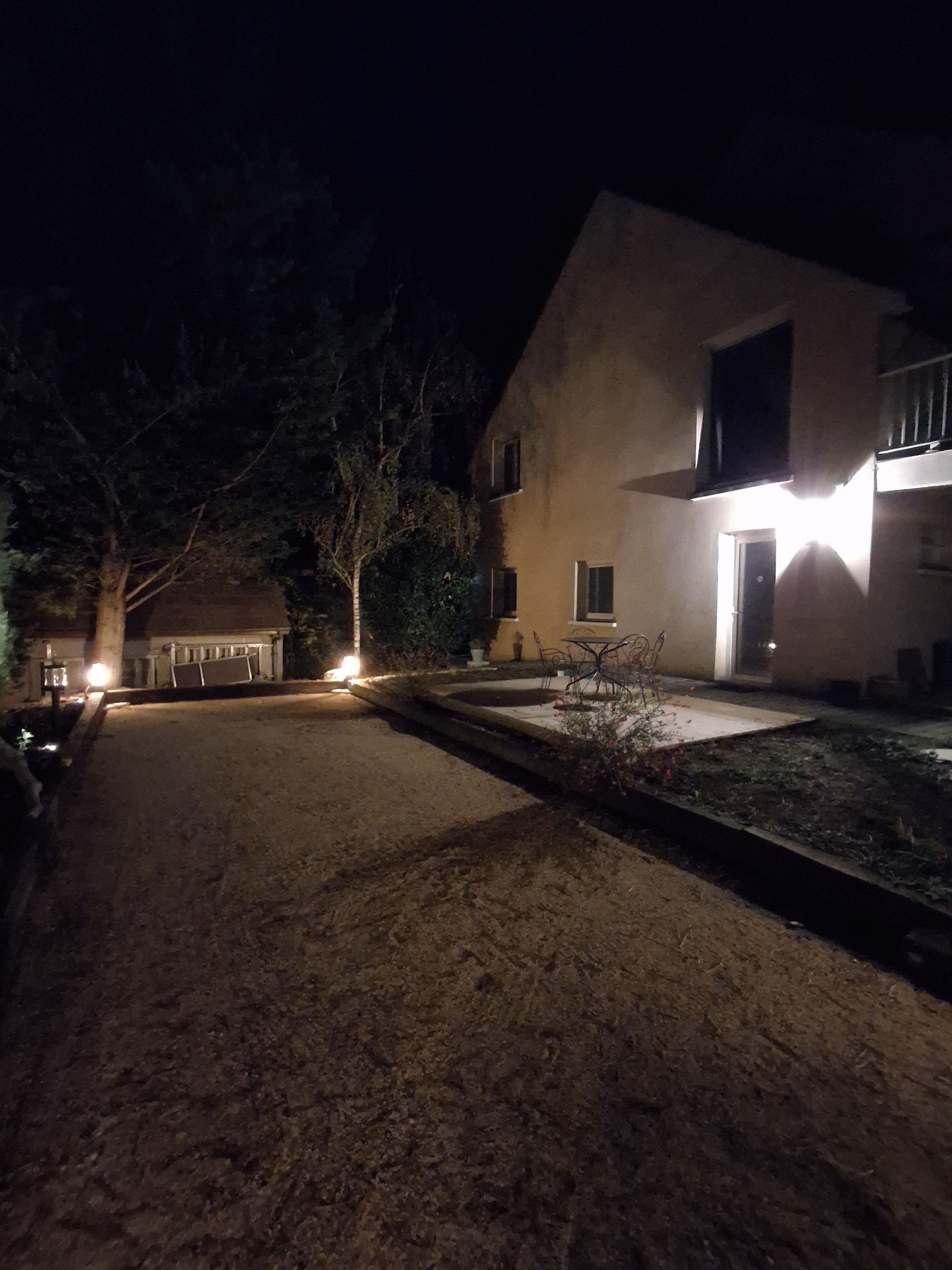 A nighttime view of a residential property with a paved driveway leading to a house with a visible door and windows.