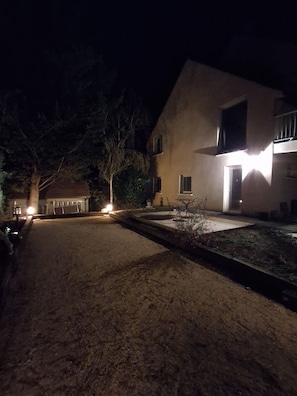 A nighttime view of a residential property with a paved driveway leading to a house with a visible door and windows.