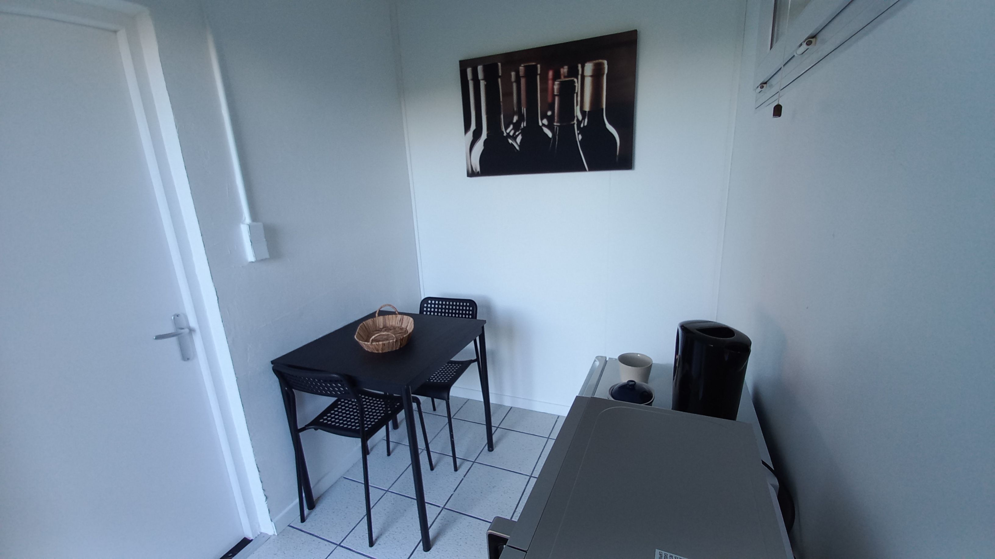 Een kleine kamer met een tafel, twee stoelen, een mandje, een waterkoker en een koffiekop.