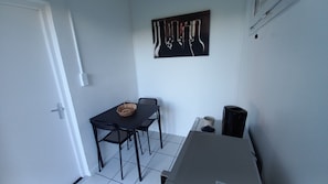 Een kleine kamer met een tafel, twee stoelen, een mandje, een waterkoker en een koffiekop.