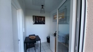 A small balcony with a table and chairs, a ceiling light fixture, and a glass door leading to a room.