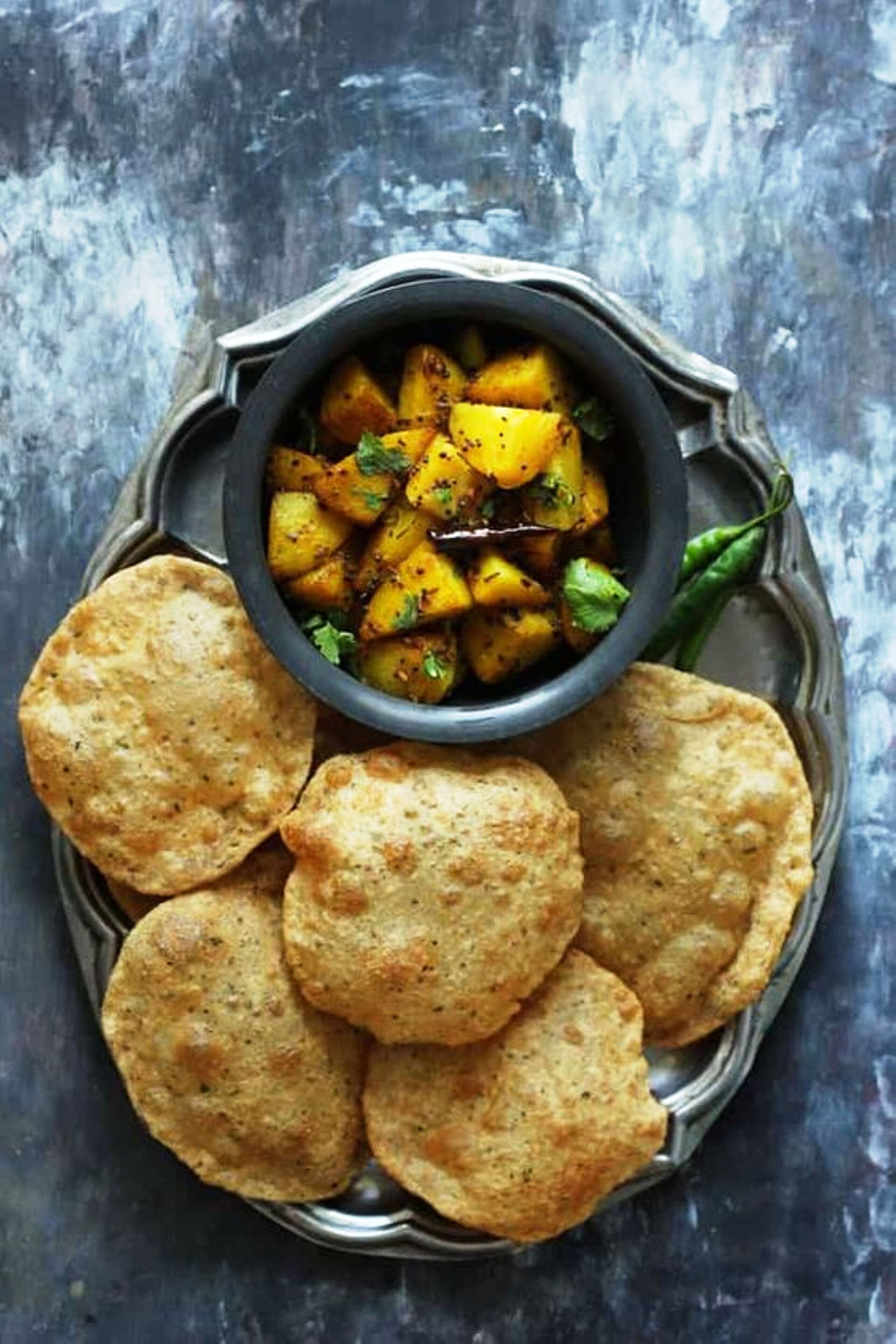 A plate with several round, golden-brown flatbreads and a bowl of seasoned potato chunks.