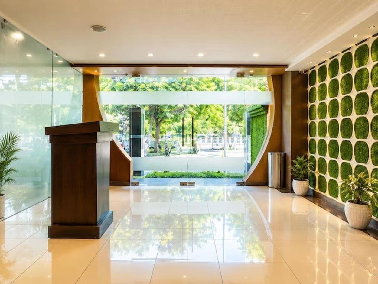 A modern lobby with a glass entrance, a wooden podium, and a green wall with a geometric pattern.
