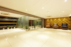 A spacious lobby with a tiled floor, potted plants, and seating areas.