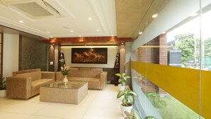 A modern lobby with a seating area, a large painting, and potted plants. - Hotel Sakura by Maps, GURGAON (Gurugram)