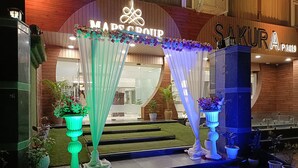 A hotel entrance with a sign reading "MADS CROFT" and "SAKURA P2019". There are decorative curtains and potted plants in front of the entrance. - Hotel Sakura by Maps, GURGAON (Gurugram)