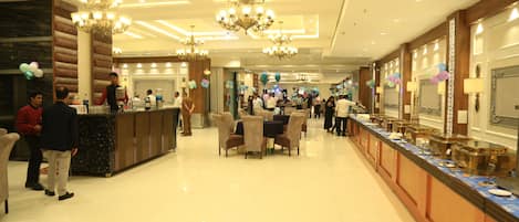 A spacious hotel lobby with a long reception desk, multiple chandeliers, and a polished floor.