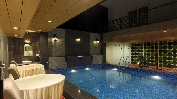 A hotel lobby with a swimming pool, seating area, and a staircase leading to an upper level. - Hotel Sakura by Maps, GURGAON (Gurugram)