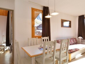 A room with a bed, a table, and chairs. There is a window with curtains, a picture on the wall, and a lamp. - Renovated 3-room apartment, ski-in/ski-out, pet-friendly (Belle Plagne)