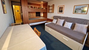 Ein kleines Zimmer mit Etagenbett, einer Schlafcouch, einem Tisch und einem Stuhl.