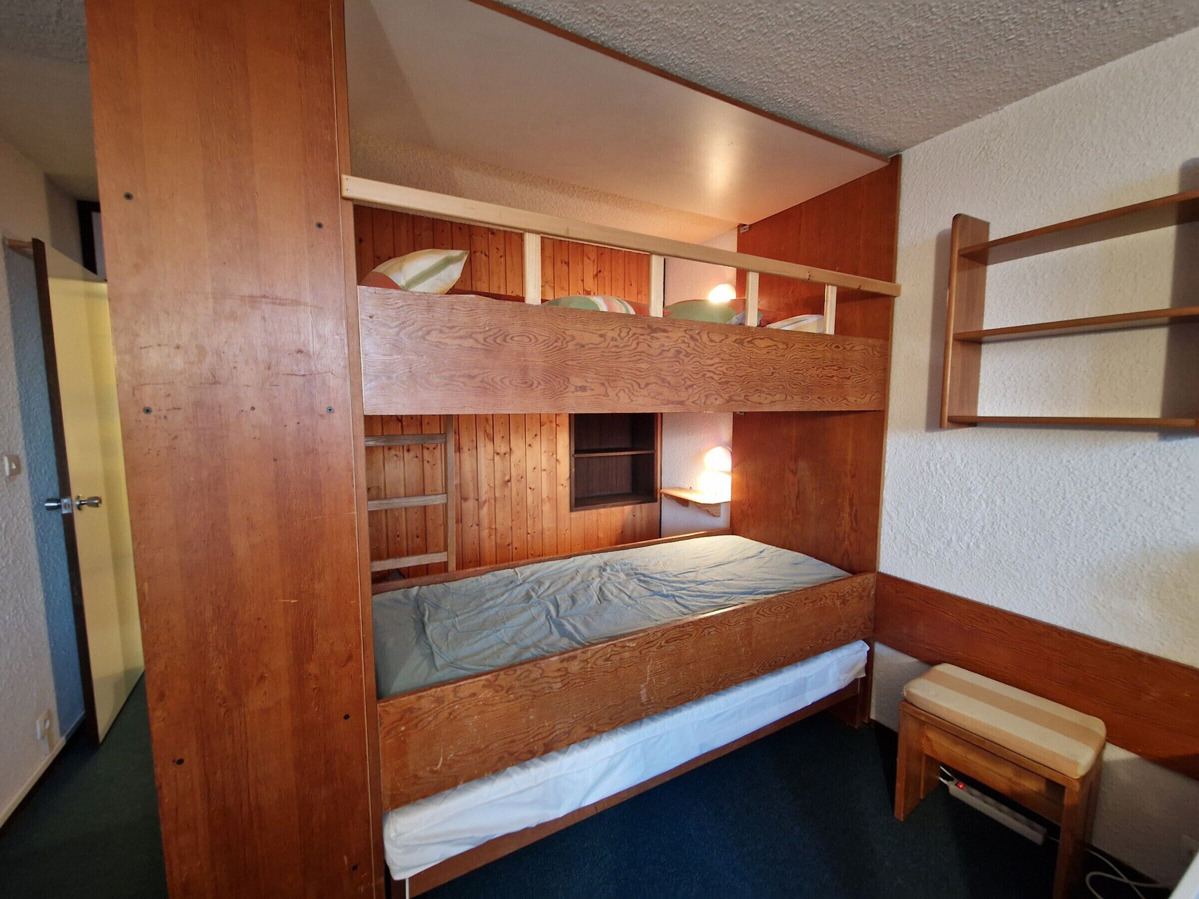 Une chambre avec un lit superposé en bois, une petite étagère et un banc.