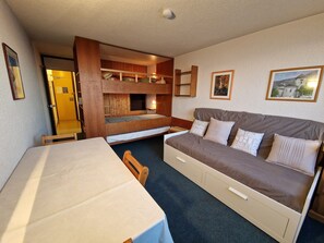 A compact room with a bunk bed, a sofa, a table, and a chair.