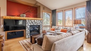 Ein Wohnzimmer mit Kamin aus Stein, einem Fernseher und einer Couch mit Kissen.