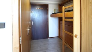 Un pasillo estrecho con una puerta de madera, una litera y un estante pequeño.