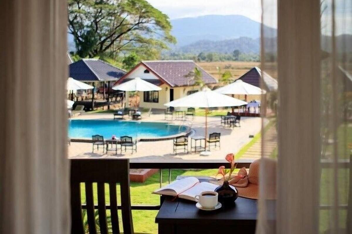 Vista di una zona piscina con ombrelloni, sedie e un libro su un tavolo.