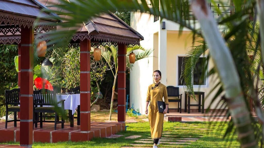 A person walking in a garden area with a gazebo, chairs, and a table.