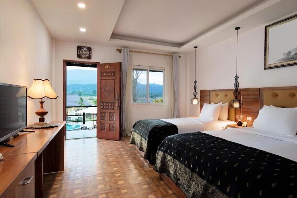 A hotel room with two beds, a desk with a lamp, a TV, and a large window with a view.