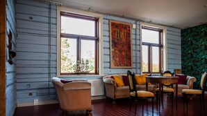 Una habitación con pisos de madera, un sofá, sillas, una mesa y ventanas grandes que dan a vistas de follaje exterior.