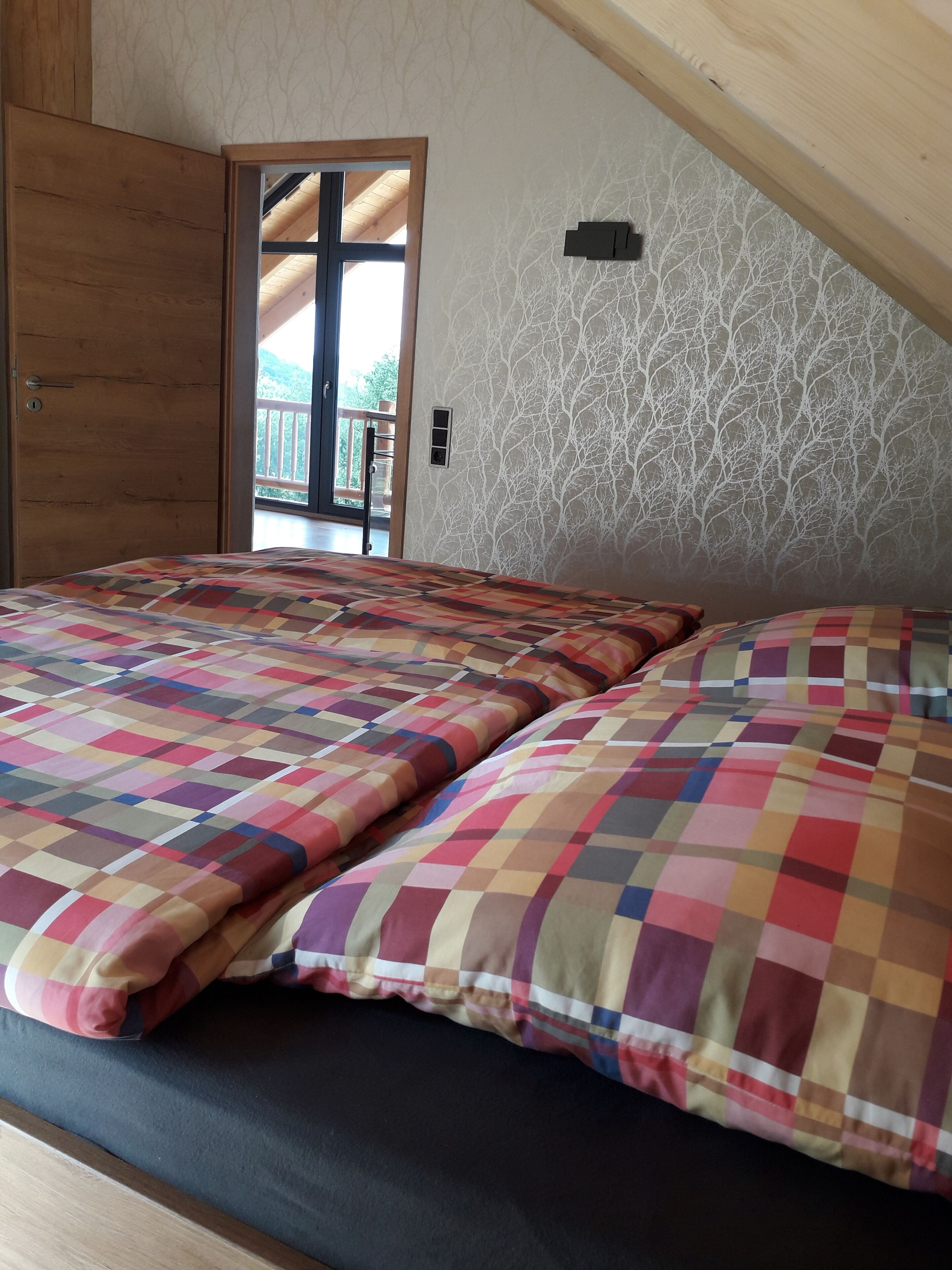 A bedroom with a checkered bedspread, a wooden door, and a view of a balcony.