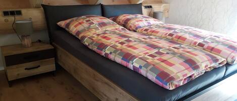 A wooden bed with a black frame and colorful checkered bedding in a room with wooden floors and sloped ceilings.