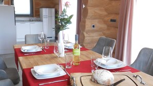 A wooden dining table set with plates, glasses, and a bottle of wine, surrounded by grey upholstered chairs. - Kanadisches Naturstamm-blockhaus (Linden)