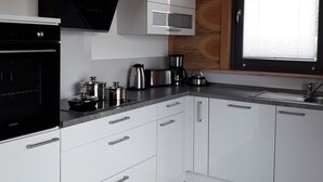 A modern kitchen with white cabinets, a black oven, a microwave, and a coffee maker. - Kanadisches Naturstamm-blockhaus (Linden)