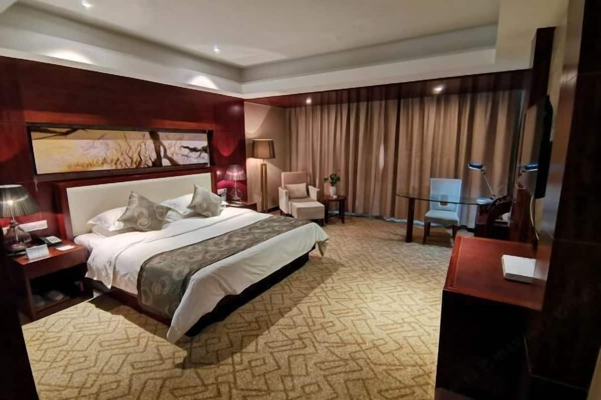 Une chambre d’hôtel avec un grand lit, un bureau, une chaise, une télévision et un tableau au mur.