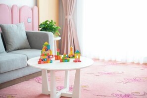 Una sala de estar acogedora con un sofá gris, una mesa de centro blanca con bloques de construcción de colores y una alfombra rosa.