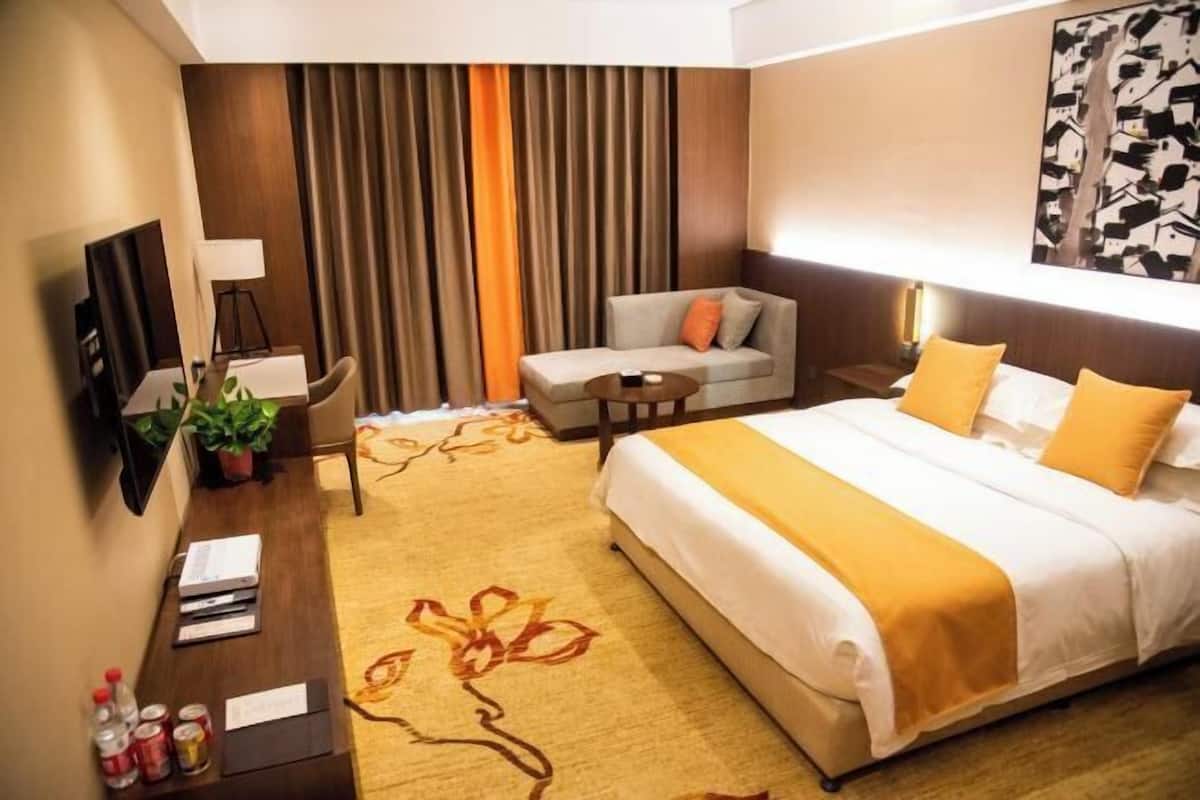 Une chambre d’hôtel avec un grand lit, un canapé, un bureau avec une lampe et une télévision.