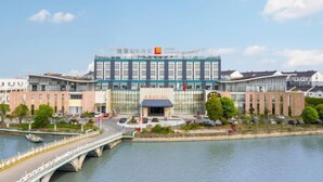 A modern building with a glass facade, a bridge in the foreground, and a river in the background. - LOUNGE GROUP (Suzhou)