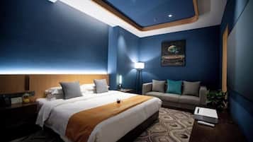 A hotel room with a bed, a sofa, a nightstand, a lamp, and a painting on the wall.