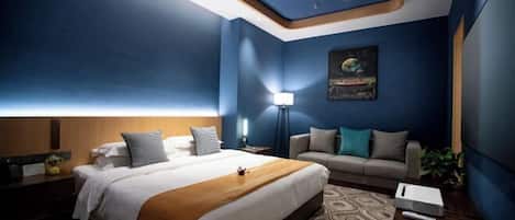 Quarto de hotel com uma cama, um sofá, uma mesa de cabeceira, um abajur e um quadro na parede.