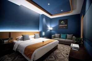 Una habitación de hotel con una cama, un sofá, una mesita de noche, una lámpara y un cuadro en la pared.
