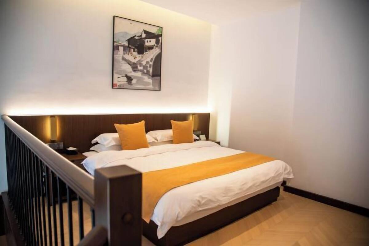 Une chambre d’hôtel avec un lit, une tête de lit, une table de chevet, une œuvre d’art accrochée au mur et un plancher en bois.
