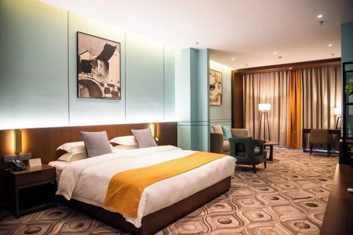 Une chambre d’hôtel avec un grand lit, un bureau, une chaise et des œuvres d’art accrochées aux murs.