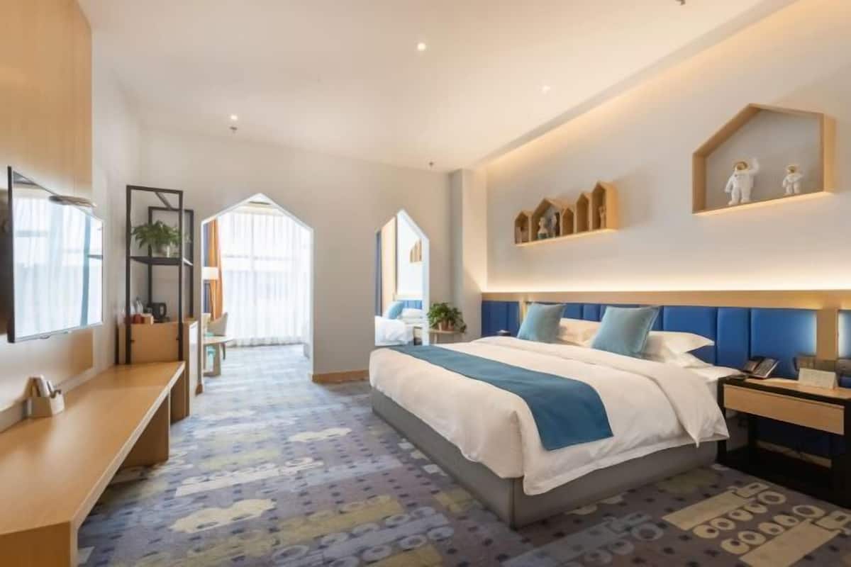 Une chambre d’hôtel moderne dotée d’un grand lit, d’un bureau et d’un coin salon. De grandes fenêtres offrent une vue sur la ville.