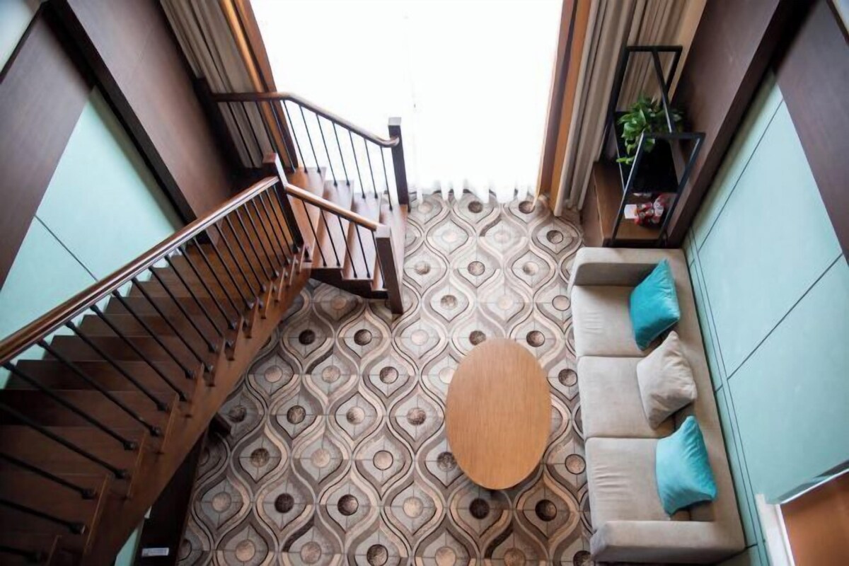 Un interior moderno con escalera de madera, suelo estampado, una mesa redonda y un sofá con cojines.
